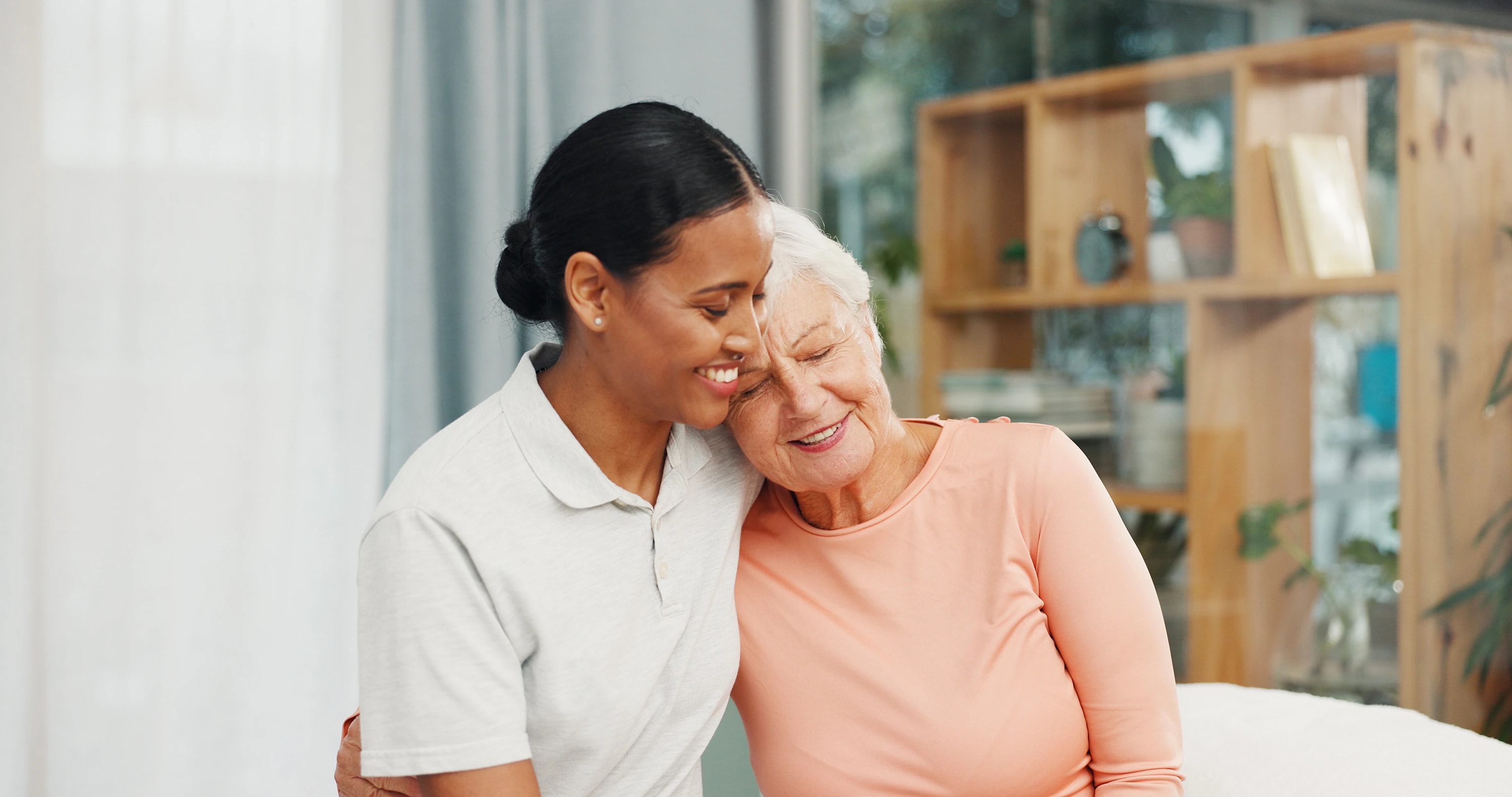 An older woman resting her head on her caregiver’s shoulder at home