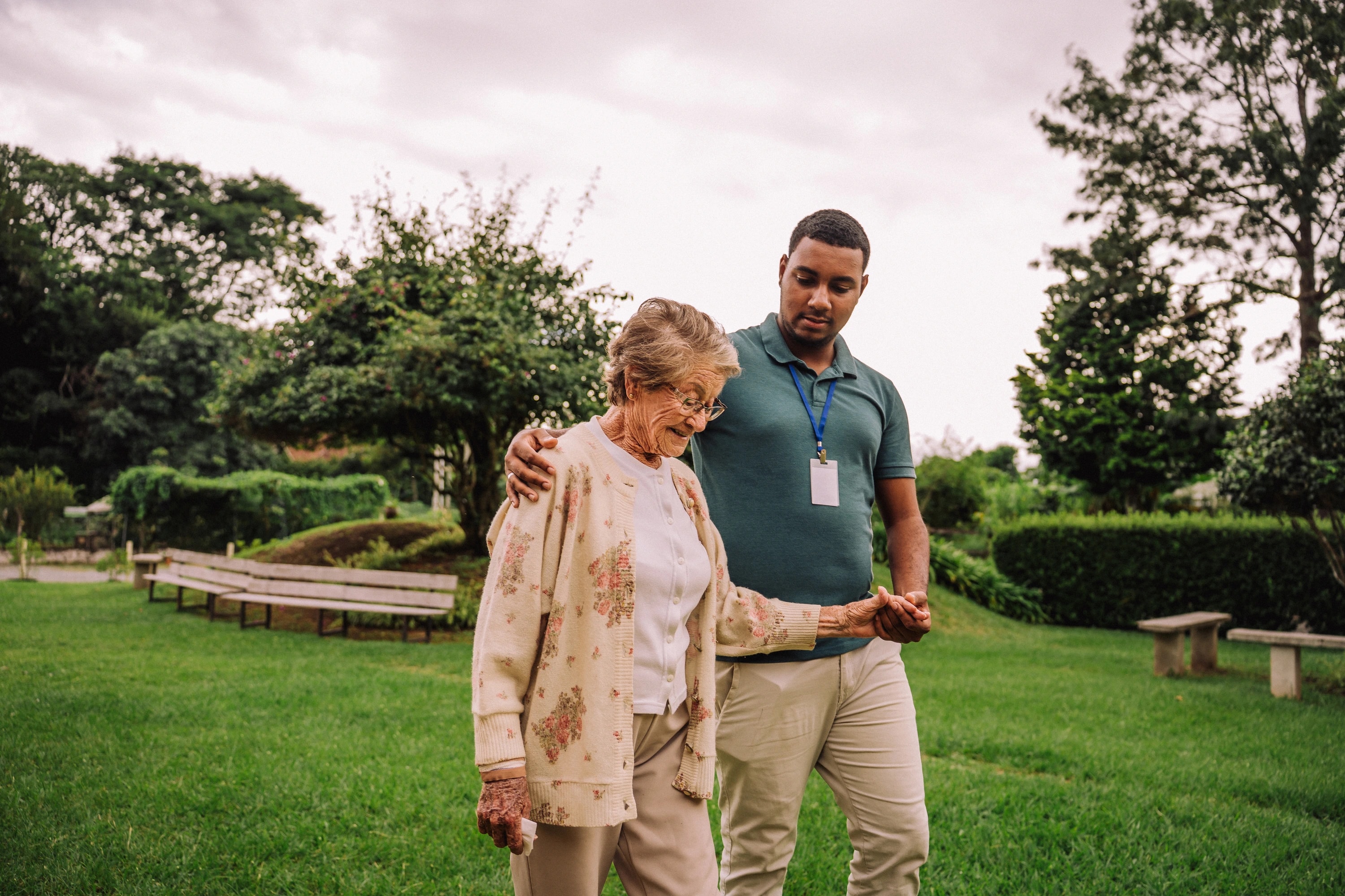 A caregiver supporting an older woman during a walk in the garden.