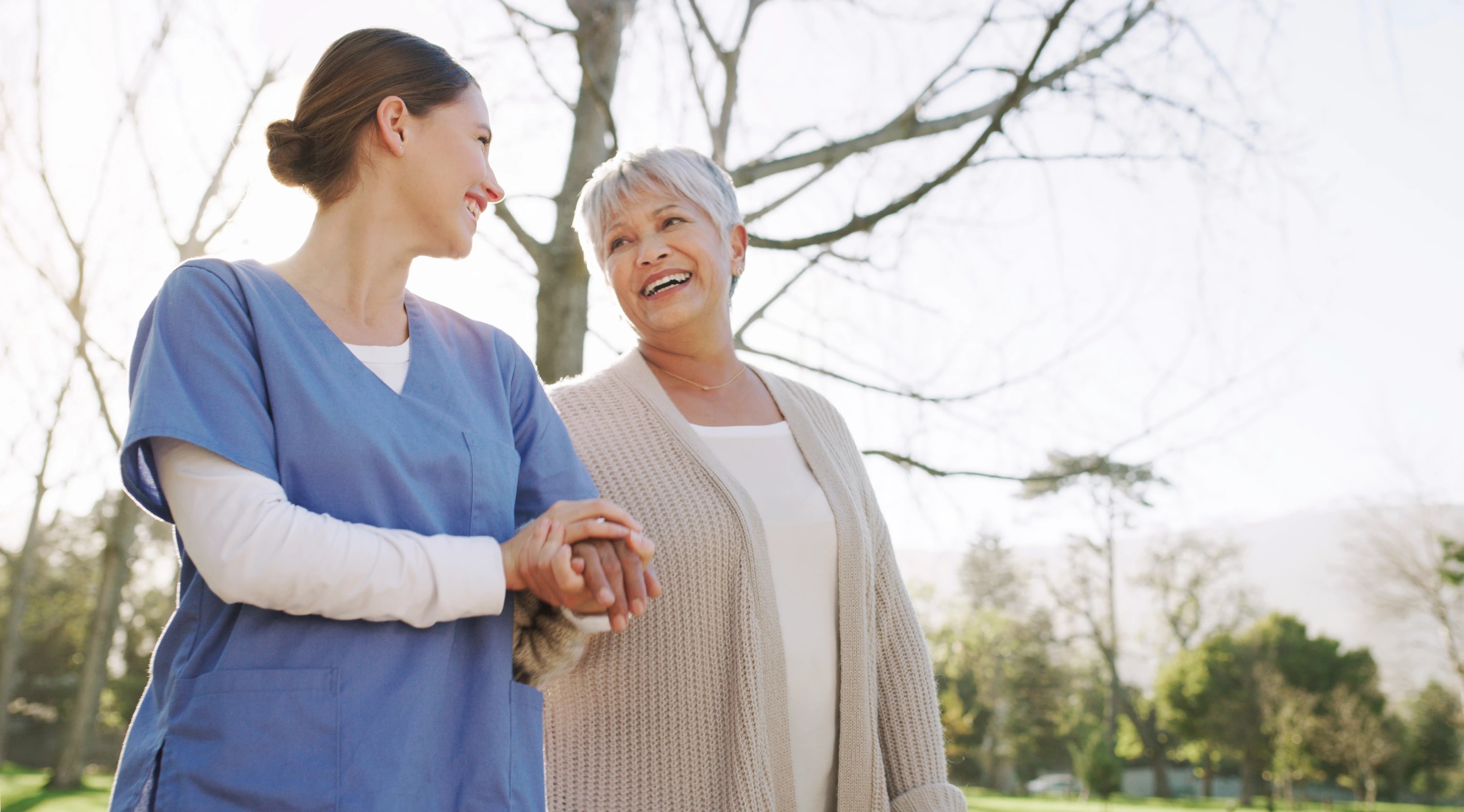 A caregiver and an older woman smiling during a walk outdoors