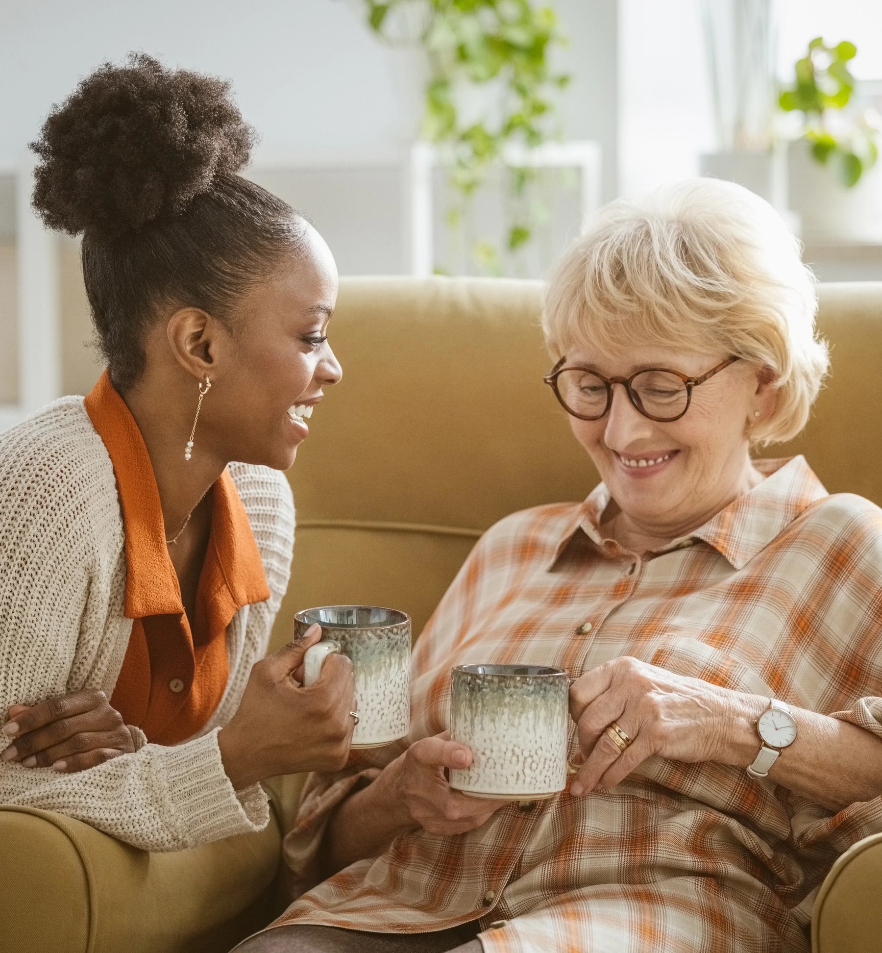 A caregiver and an older woman sharing a relaxed conversation over mugs at home