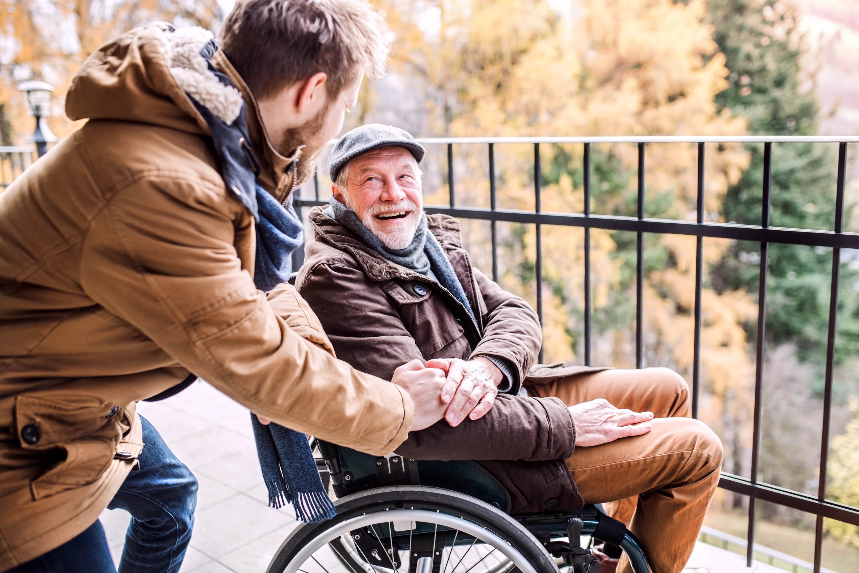 A younger man and an older man in a wheelchair enjoying a moment together on a balcony